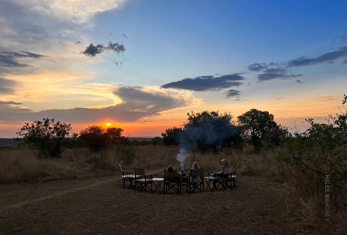 safari guests enjoy sundowners at the campfire in serengeti