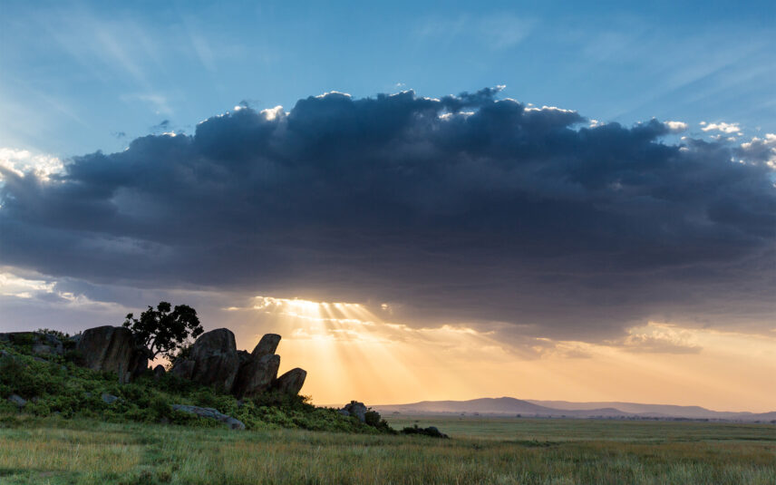 sun shines through cloud over kopje in serengeti
