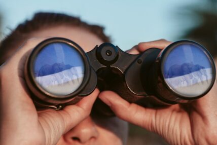 person looking at elephants through binoculars on safari