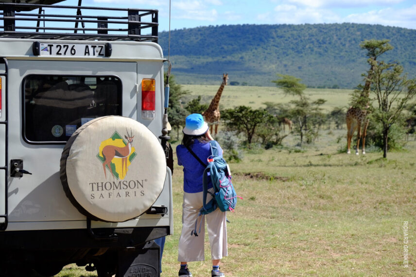 woman next to thomson rover looking at giraffes in tanzania