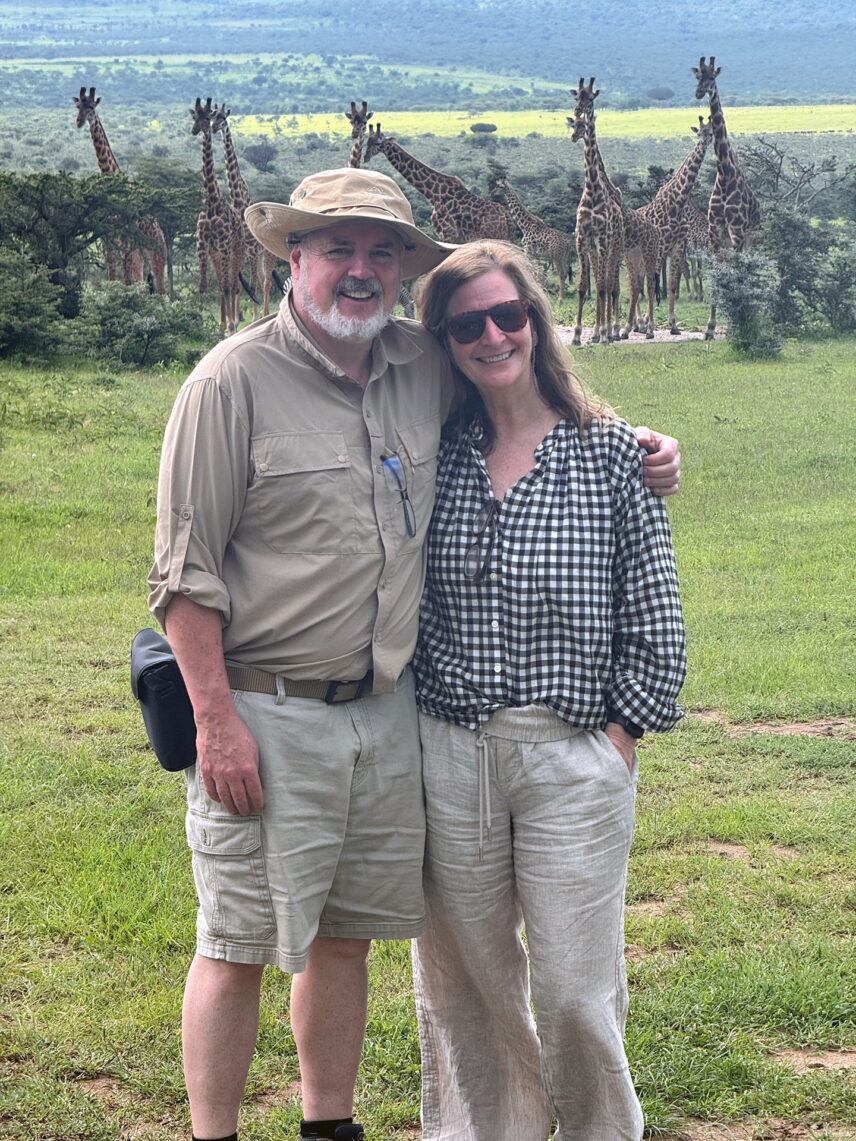 couple at eastern serengeti nature refuge waterhole with multiple giraffes